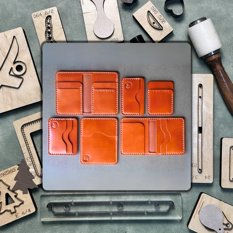 May include: An assortment of orange leather wallets and cardholders with white stitching. The wallets are arranged on a gray surface, surrounded by leather crafting tools and wooden stamps. The wallets have the text "LOW TIDE" on them.
