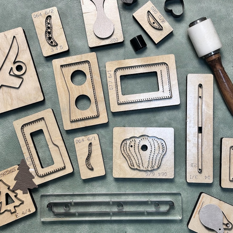 May include: A collection of various wooden leathercraft cutting dies, including shapes like rectangles, ovals, and organic forms. Some dies have numbers and letters printed on them, such as "064 6/2" and "345". A mallet is also present.