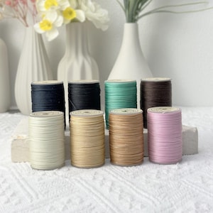 以下が含まれることがあります： 黒、白、ベージュ、茶色、ピンク、緑など、さまざまな色の糸巻きが8つあります。糸巻きは4つずつ2列に並べてあり、後ろの列の糸巻きは前の列の糸巻きよりも少し高くなっています。