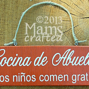 May include: A rustic wooden sign with a red background and white text. The sign reads "Cocina de Abuelo Los ni&ntilde;os comen gratis".