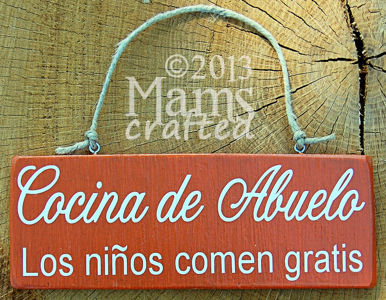 May include: A rustic wooden sign with a red background and white text. The sign reads "Cocina de Abuelo Los ni&ntilde;os comen gratis".