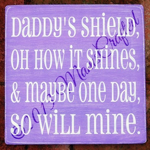 May include: Purple wooden sign with white text that reads "Daddy's shield, oh how it shines, & maybe one day, so will mine."