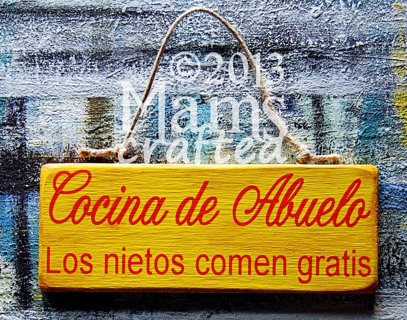 May include: A yellow wooden sign with red text that reads "Cocina de Abuelo Los nietos comen gratis". The sign is hanging from a string.