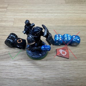 May include: A miniature black and silver figurine of a warrior with a blue weapon, a black die with white numbers, and three blue dice with white dots. The figurine is on a green base.