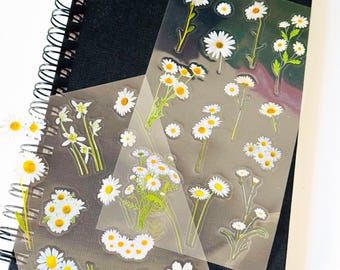 Peut inclure: Deux feuilles de papier autocollant transparent avec des motifs de marguerites blanches. Les autocollants sont disposés en rangées et en colonnes sur les feuilles.