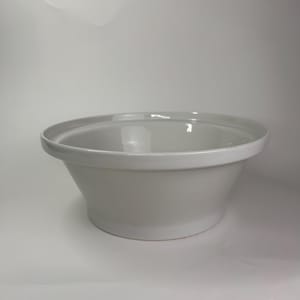 May include: A white ceramic bowl with a wide rim and a gently sloping body. The bowl has a smooth, glossy finish and is likely used for serving or mixing food. The design is simple and elegant, suitable for various kitchen styles.