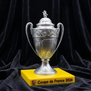 Peut inclure: Un trophée argenté avec couvercle et anses, posé sur un socle jaune. Le trophée présente des détails complexes et une petite figurine sur le dessus. Le socle porte l'inscription "Coupe de France 2026".