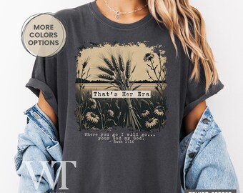 May include: Dark grey t-shirt with a wheat and floral graphic. The text "That's Her Era" is above a quote from Ruth 1:16. The shirt is a pepper color.