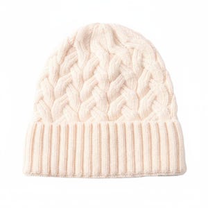 May include: Cream-colored cable knit beanie hat. The hat features a ribbed brim and a textured cable knit pattern across the crown. The hat is made of a soft, warm material, perfect for cold weather. The hat is a neutral color, making it versatile for any outfit.