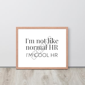 May include: A framed print with the text "I'm not like normal HR I'm cool HR" in black font on a white background. The frame is light brown wood.