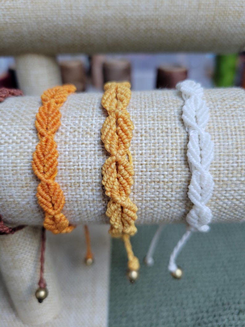 Pu&ograve; includere: Tre braccialetti dell'amicizia in arancione, giallo e bianco. I braccialetti sono realizzati con un cordoncino annodato e hanno una piccola perla all'estremit&agrave;.