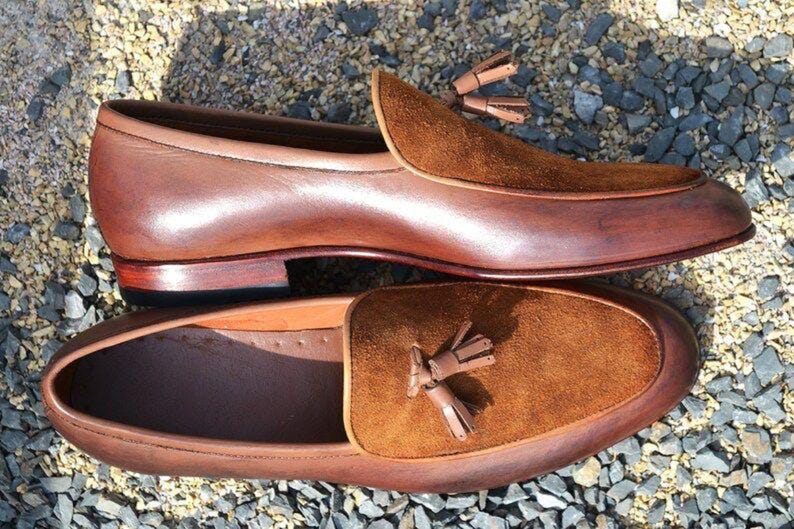 Peut inclure: Une paire de mocassins en cuir marron avec des accents en daim et des glands. Les mocassins ont une semelle en cuir marron et un talon en cuir marron.