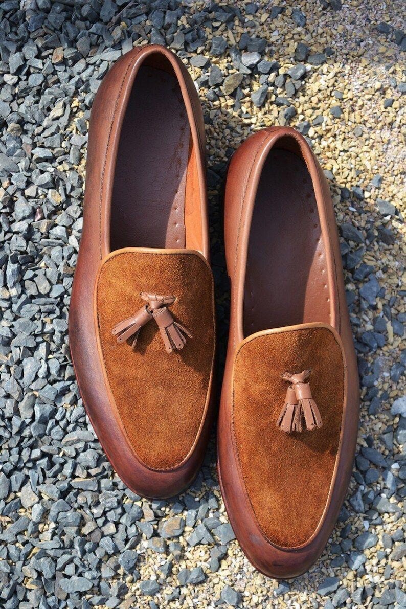 Peut inclure: Une paire de mocassins en cuir marron avec des glands en daim. Les mocassins ont une semelle en caoutchouc et sont pos&eacute;s sur un lit de gravier.