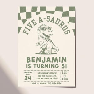 Op de afbeelding: Een beige verjaardagsuitnodiging met een cartoon-dinosaurus met een zonnebril. De tekst luidt "FIVE A-SAURUS" boven de dinosaurus en "BENJAMIN IS TURNING 5!" eronder. Bevat datum, tijd en locatie.
