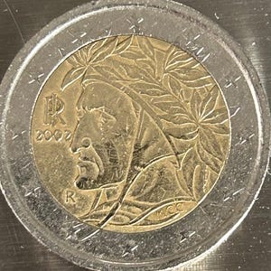 Puede incluir: Una moneda italiana de 2 euros de 2002 de color plateado y dorado que presenta el perfil de un hombre con una corona de laurel en la cabeza. La moneda tiene la letra "R" y el año "2002" en el lado izquierdo. La moneda también tiene las letras "RI" y "R" en el lado derecho.