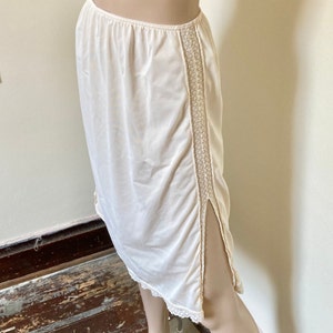 May include: A white slip skirt with a lace trim along the sides and bottom. The skirt has a slit up the side.