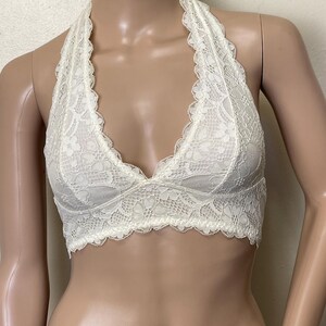 Pu&ograve; includere: Bralette color avorio con un delicato motivo floreale in pizzo. Il bralette &egrave; in stile halter. Il bordo smerlato adorna lo scollo e l'orlo inferiore. Il tessuto sembra morbido e leggero, adatto da indossare da solo o a strati.