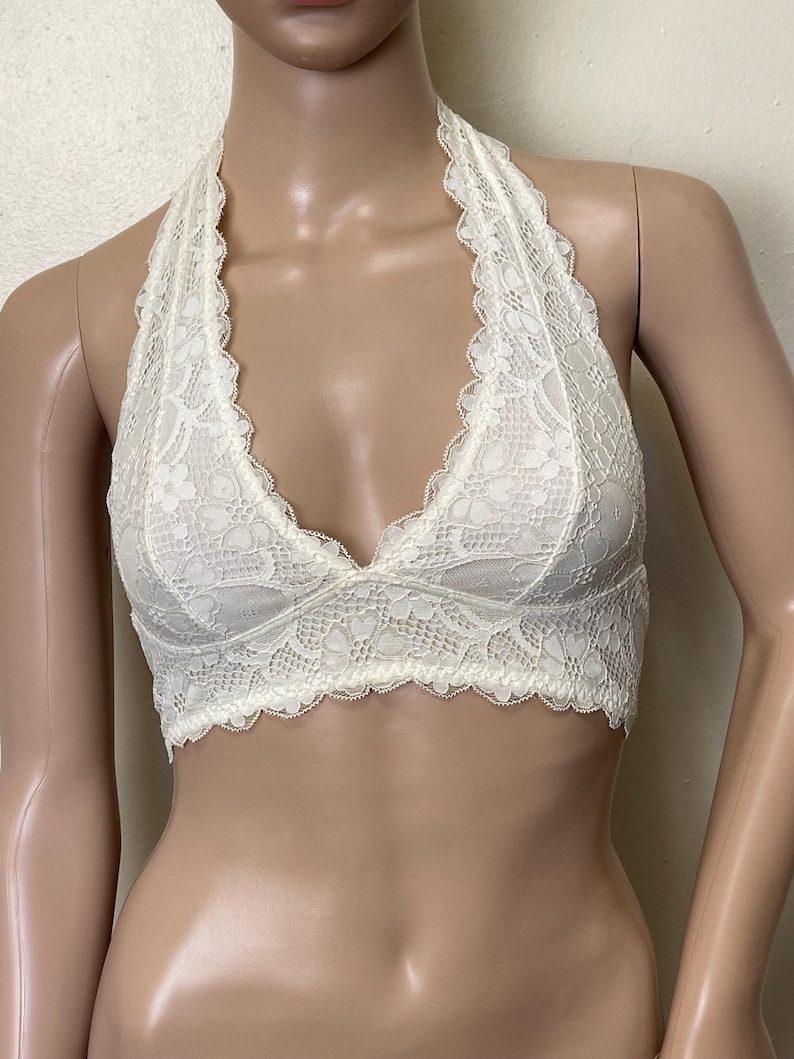 Pu&ograve; includere: Bralette color avorio con un delicato motivo floreale in pizzo. Il bralette &egrave; in stile halter. Il bordo smerlato adorna lo scollo e l'orlo inferiore. Il tessuto sembra morbido e leggero, adatto da indossare da solo o a strati.