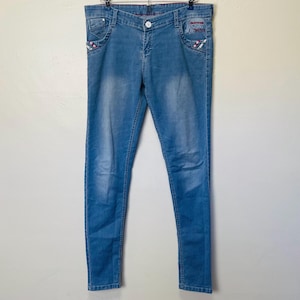 May include: Light blue denim jeans with embroidered details on the pockets. The jeans have a slim fit and a straight leg.