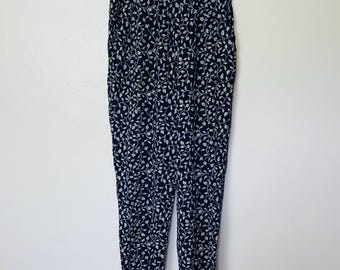 Puede incluir: Pantalón negro con estampado floral blanco. El pantalón tiene un corte holgado y una longitud ligeramente recortada.