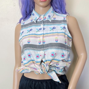 Może przedstawiać: Koszula bez rękawów zapinana na guziki w kolorowe pasy z motywem kwiatów, konewek i narzędzi ogrodniczych. Koszula jest zawiązana w talii.