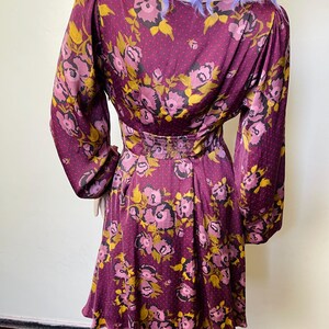 May include: A maroon dress with a floral print in shades of pink and yellow. The dress has long sleeves and a fitted bodice. The skirt is a-line and falls to just above the knee.