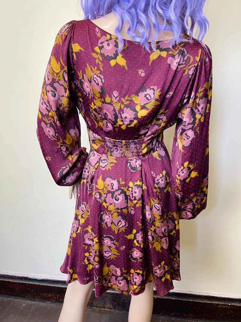 May include: A maroon dress with a floral print in shades of pink and yellow. The dress has long sleeves and a fitted bodice. The skirt is a-line and falls to just above the knee.