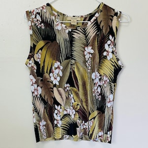 Puede incluir: Top sin mangas con estampado floral tropical. El top presenta un fondo negro con hojas grandes en tonos verdes, marrones y beige, y flores blancas. El top está colgado de una percha blanca.