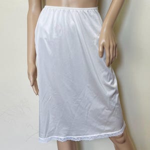 May include: A white slip skirt with a lace trim. The skirt is made of a silky material and has a simple, classic design.