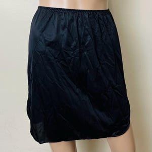 May include: A black slip skirt made of a silky material. The skirt is knee-length and has a simple, classic design.