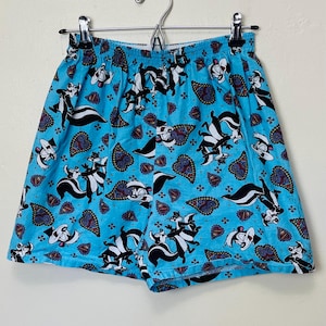 Könnte beinhalten: Hellblaue Boxershorts mit einem Allover-Print mit Cartoon-Stinktieren und Paisley-Mustern. Die Shorts haben einen elastischen Bund und hängen an einem Metallbügel.