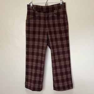 May include: A pair of vintage, high-waisted trousers in a burgundy and tan plaid pattern. The pants have a straight leg cut, two front pockets, and a button closure. The fabric appears to be a medium-weight material.