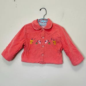 May include: A pink corduroy jacket with a white collar and embroidered animals playing musical instruments.