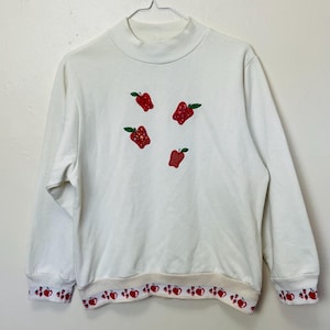 Puede incluir: Una taza de cerámica blanca con un asa negra y el texto "But First, Coffee" en un estilo manuscrito. La taza está sobre una superficie blanca. La taza mide aproximadamente 10 cm de alto.