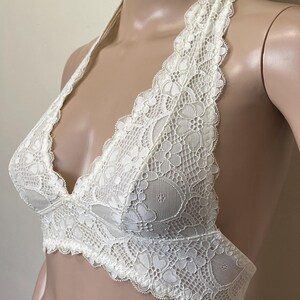 Pu&ograve; includere: Reggiseno all'americana in pizzo color avorio con un delicato motivo floreale. Il reggiseno presenta una profonda scollatura a V e bordi smerlati, offrendo un design femminile ed elegante. Il reggiseno &egrave; esposto su un manichino.