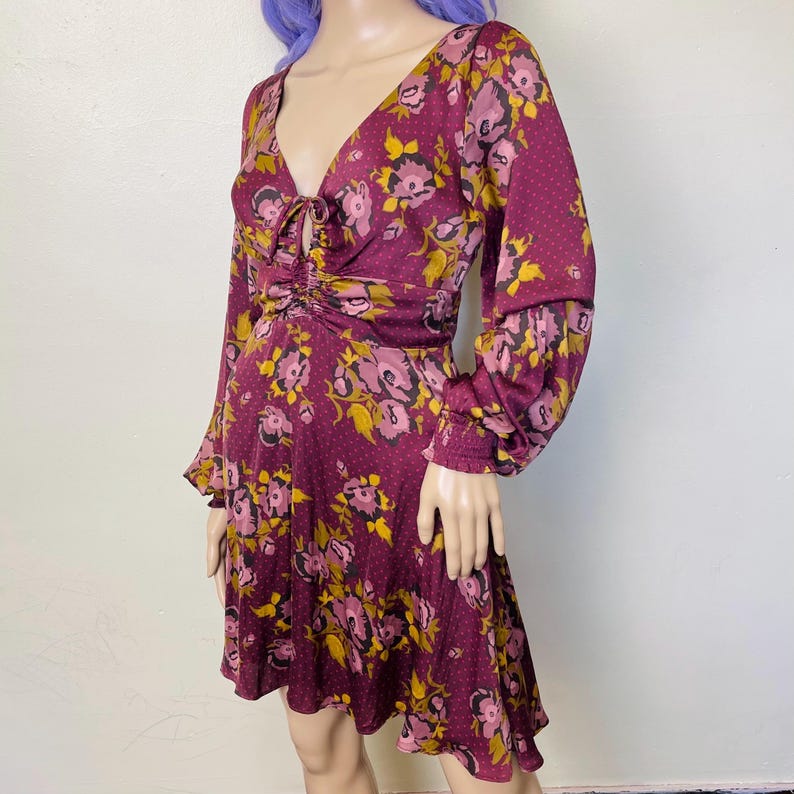 May include: A burgundy floral print dress with long sleeves and a V-neck. The dress has a cinched waist and a flowing skirt.