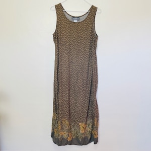 May include: A sleeveless, floor-length dress with a brown and tan speckled pattern. The bottom hem features a floral design in shades of brown, green, and yellow. The dress is hanging on a white hanger against a white background.