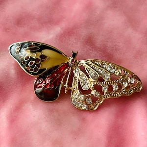 May include: A gold butterfly brooch with red, white, and black enamel wings and a clear rhinestone body.