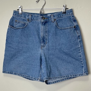 May include: Light blue denim shorts with a classic five-pocket design. The shorts have a button and zipper closure, belt loops, and a slightly faded wash. They are hanging on a metal hanger against a neutral background.