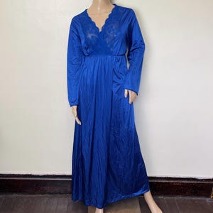 May include: A long, royal blue nightgown with long sleeves. The V-neckline features a delicate lace insert. The gown has a fitted waist and a flowing skirt, creating an elegant silhouette. The fabric has a subtle sheen.