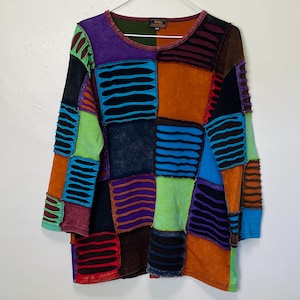 Pode incluir: Uma camisa de manga comprida em patchwork multicolorido com gola redonda. A camisa é feita de diferentes tecidos e tem um visual desgastado. A camisa é uma mistura de laranja, verde, azul, roxo e preto.