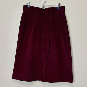 May include: A burgundy corduroy skirt with a high waist and pleats. The skirt has a button closure and pockets.