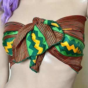 May include: A green, orange and yellow patterned scarf tied around a mannequin's neck. The scarf has a zig-zag pattern with a thin orange stripe.