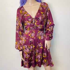 May include: A burgundy floral print dress with long sleeves and a cinched waist. The dress has a V-neckline and a tie detail at the neckline.