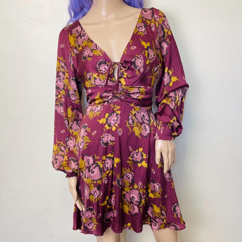 May include: A burgundy floral print dress with long sleeves and a cinched waist. The dress has a V-neckline and a tie detail at the neckline.