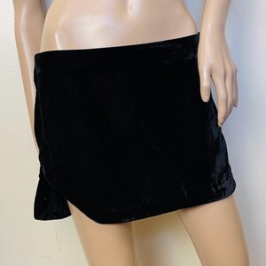 May include: A black velvet mini skirt with a side slit. The skirt is fitted and has a smooth, silky texture.