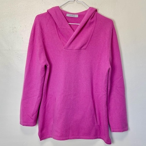 Puede incluir: Un suéter rosa con capucha, cuello de pico y un bolsillo en la parte delantera. El suéter está hecho de un tejido suave y de punto.