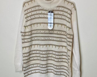 May include: A white sweater with a high neck and brown and gold striped pattern. The sweater is decorated with gold beads and has a tag that reads "Victoria Harbour".