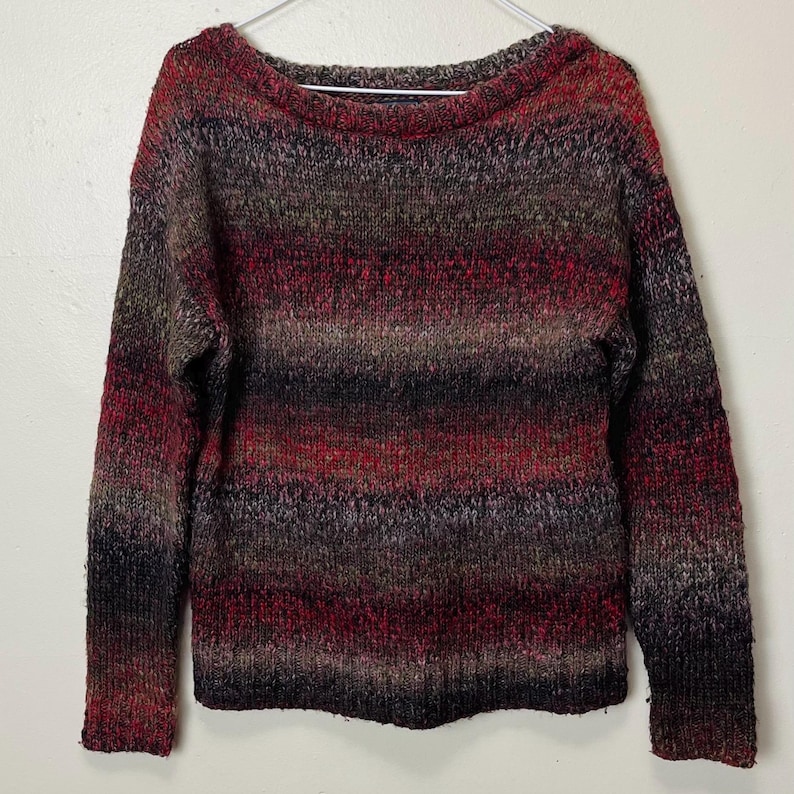 May include: A multi-colored sweater with a boat neck. The sweater features horizontal stripes in shades of red, brown, black, and gray. The long-sleeved sweater is hanging on a white hanger.