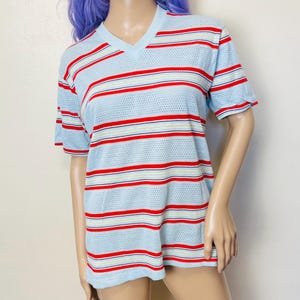 May include: A light blue striped t-shirt with red, white, and blue stripes. The shirt has a v-neck and short sleeves.